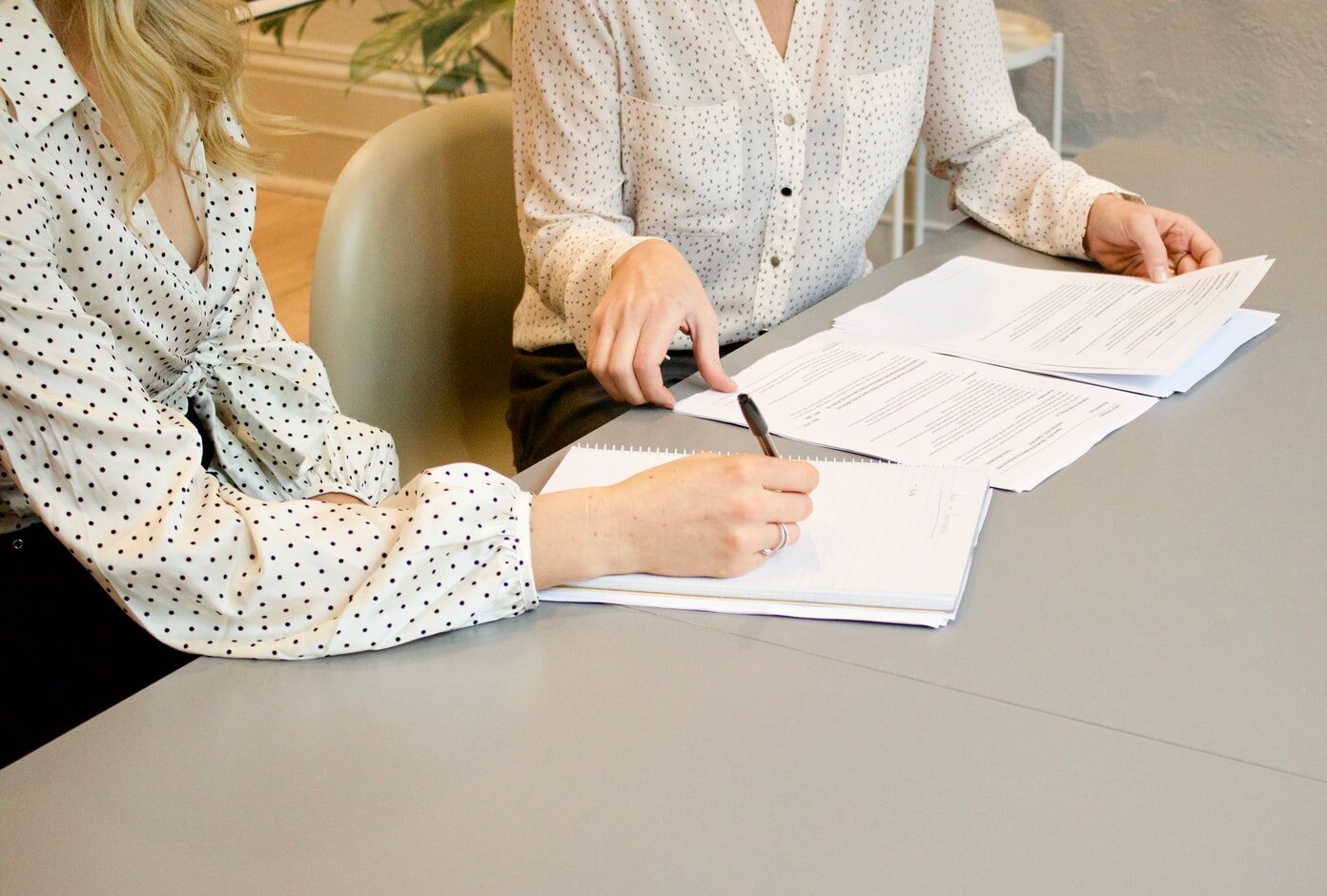 woman signing on white printer paper beside woman about to touch the documents